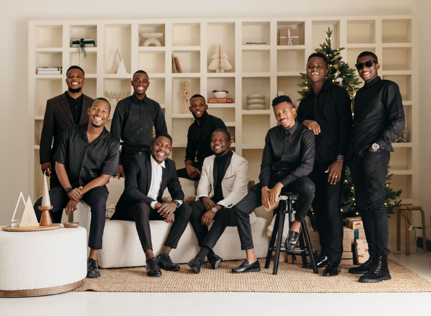 Group in coordinated black outfits pose together in front of white built-in shelves in a modern interior setting.