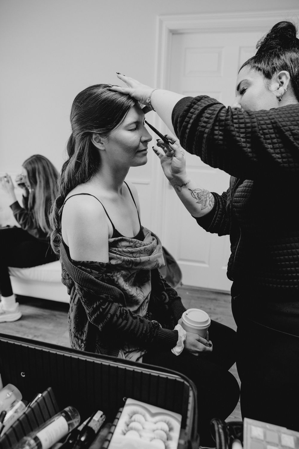 Black and white photo of makeup artist applying eye makeup to brunette bride before wedding.