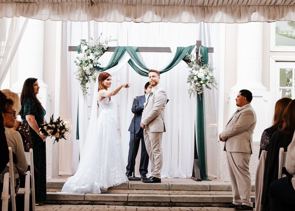 Bride playfully touches grooms face at the altar during their wedding ceremony under a draped arch.