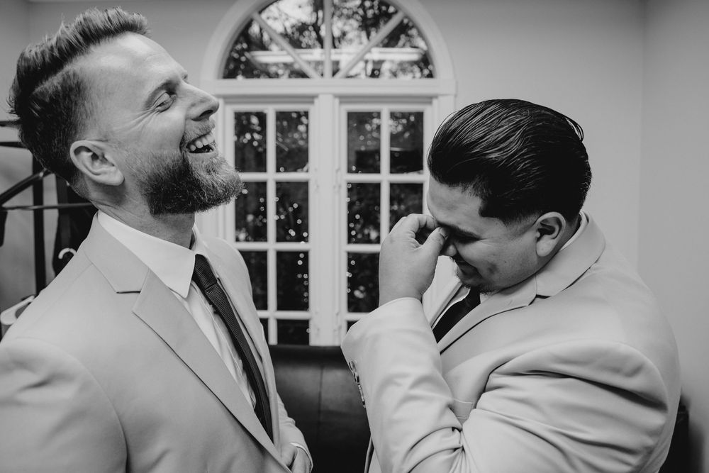 Two grooms share a heartfelt emotional moment, one wiping tears, before their wedding ceremony.