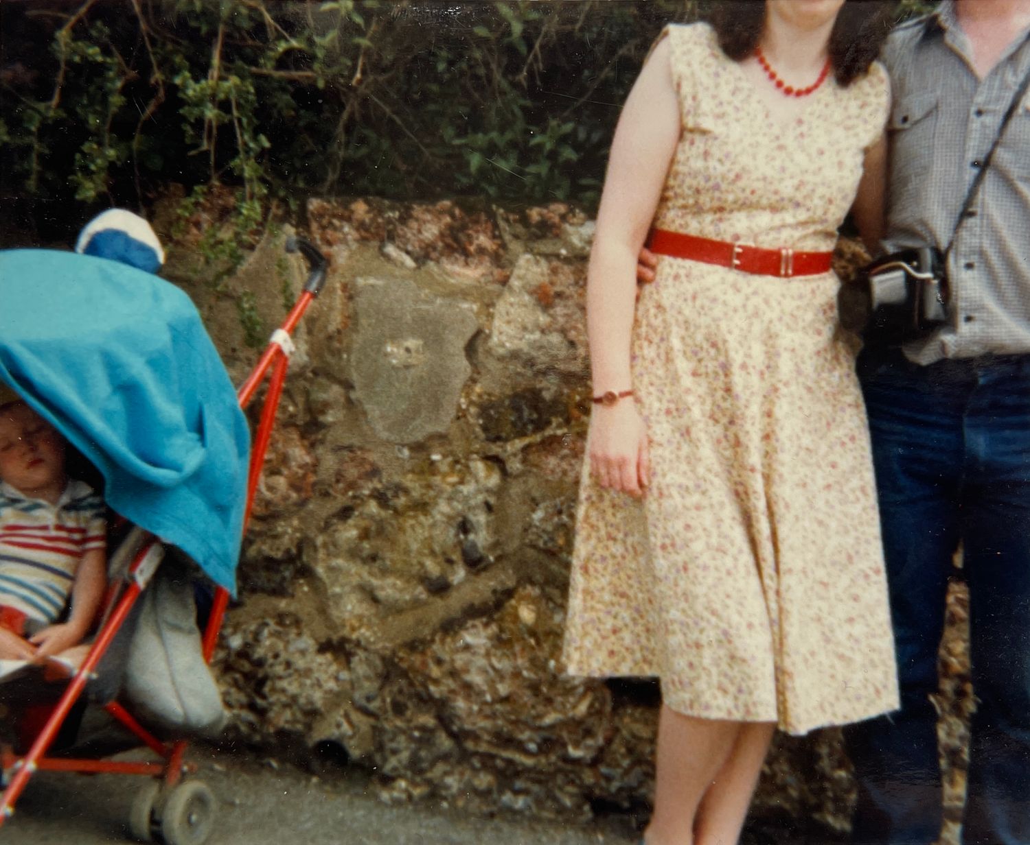Vintage photograph showing a cream lace dress with red belt against a stone wall.