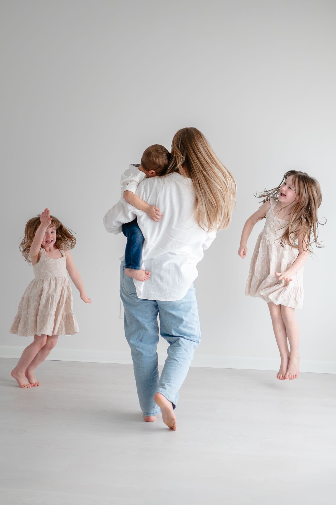 Happy family in casual clothing dancing and playing together against white wall in bright minimalist setting.