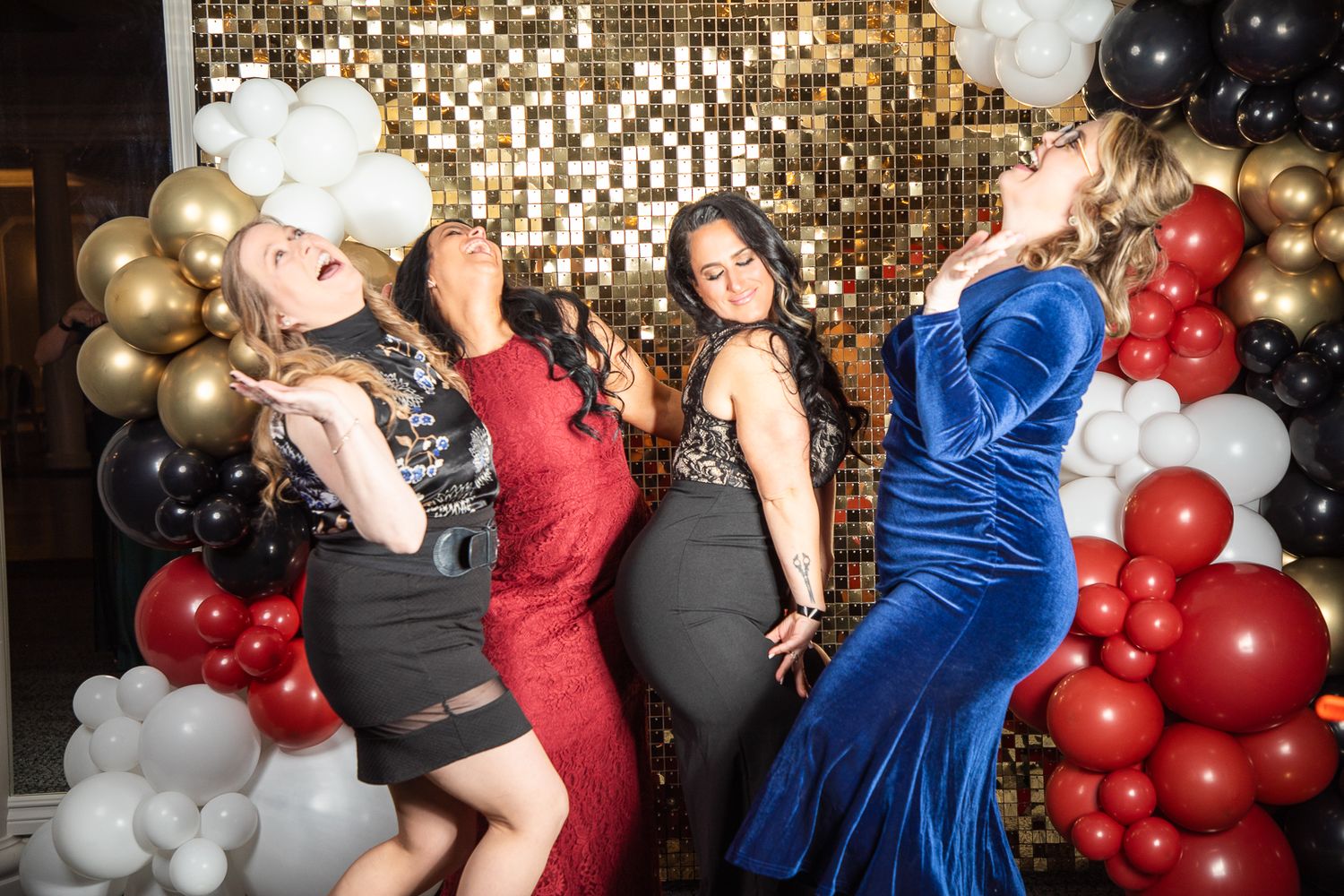Party scene with balloon arch featuring red, black, gold and white balloons against sparkly backdrop.