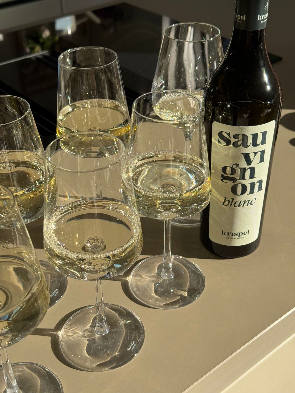 Multiple wine glasses filled with Sauvignon Blanc white wine beside a Kaspel bottle on a countertop.