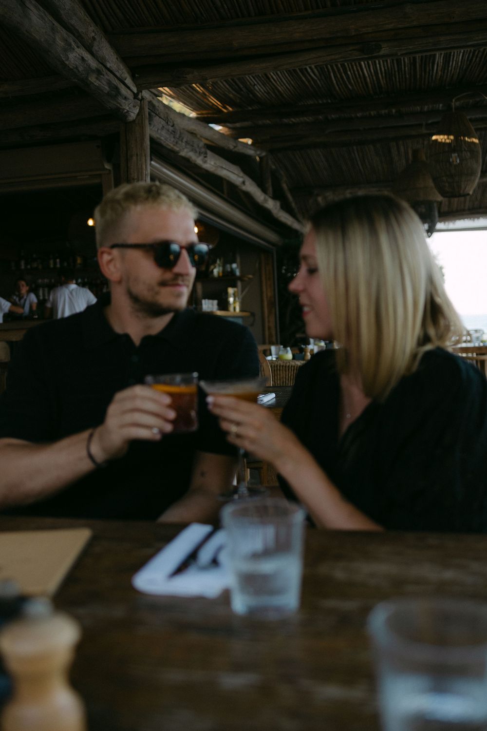 Couple clinking beer glasses together at a rustic wooden bar restaurant on a date.