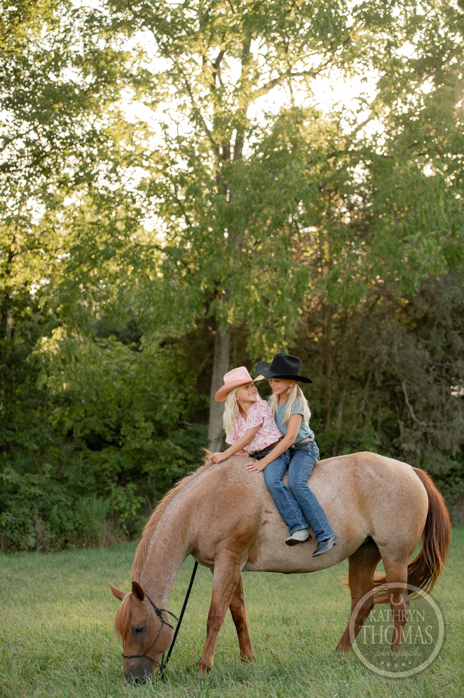 Two riders sharing a moment on horseback while their horse grazes at sunset.