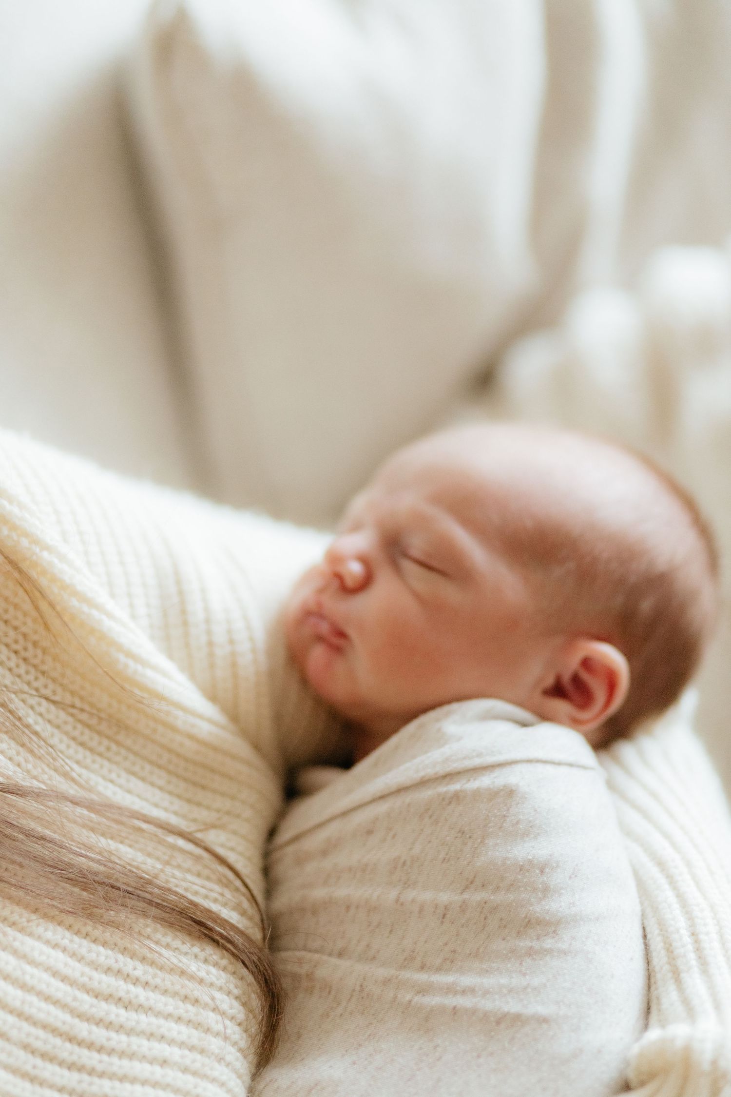 A peaceful newborn baby sleeps snugly wrapped in a soft cream-colored blanket.