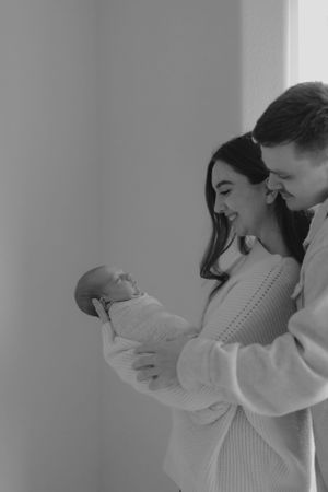 A tender black and white moment showing new parents sharing joyful laughter while holding their newborn baby.