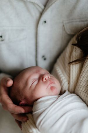 A sleeping newborn baby in white clothing rests peacefully against a cream-colored blanket.