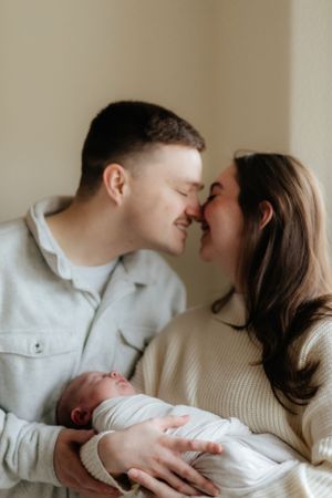 A tender moment between parents as they cradle their sleeping newborn baby dressed in white.