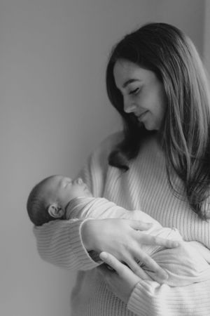 A tender black and white portrait showing a gentle moment between parent and newborn baby.