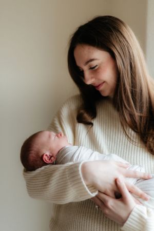 A tender moment captured as someone wearing a cream sweater cradles a sleeping newborn baby against a light background.