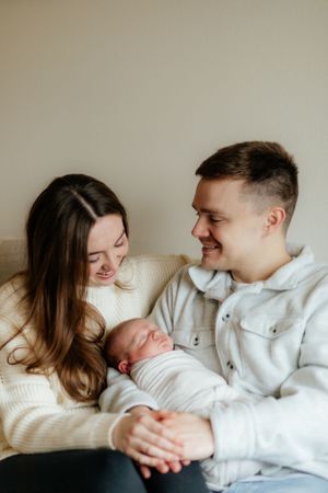 A couple in cozy sweaters share a joyful moment with their newborn baby on the couch.