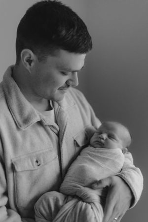 A tender black and white portrait of a parent in a light-colored jacket holding a sleeping newborn baby.