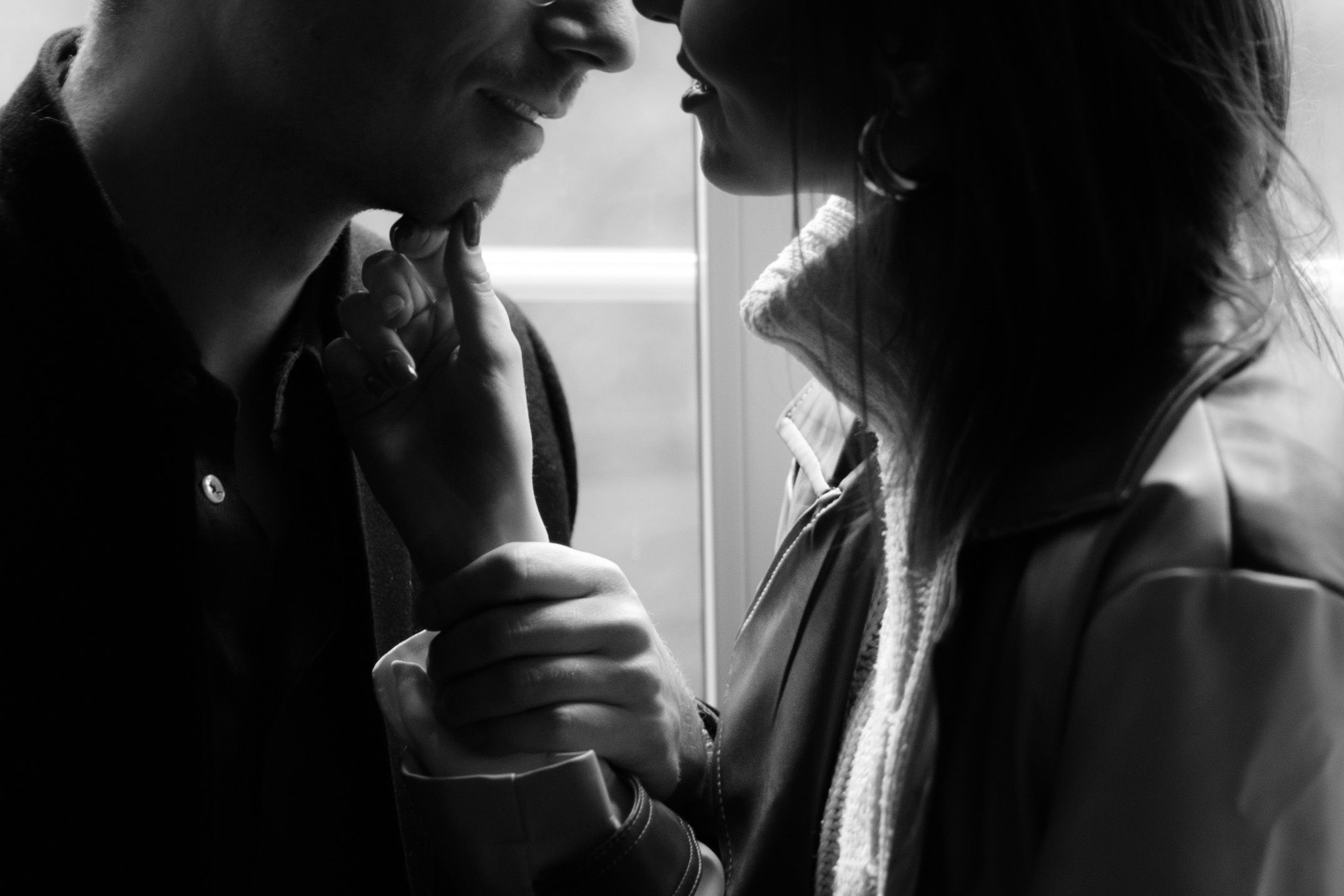 Silhouetted figures in a dramatic black and white intimate moment with light streaming through window.
