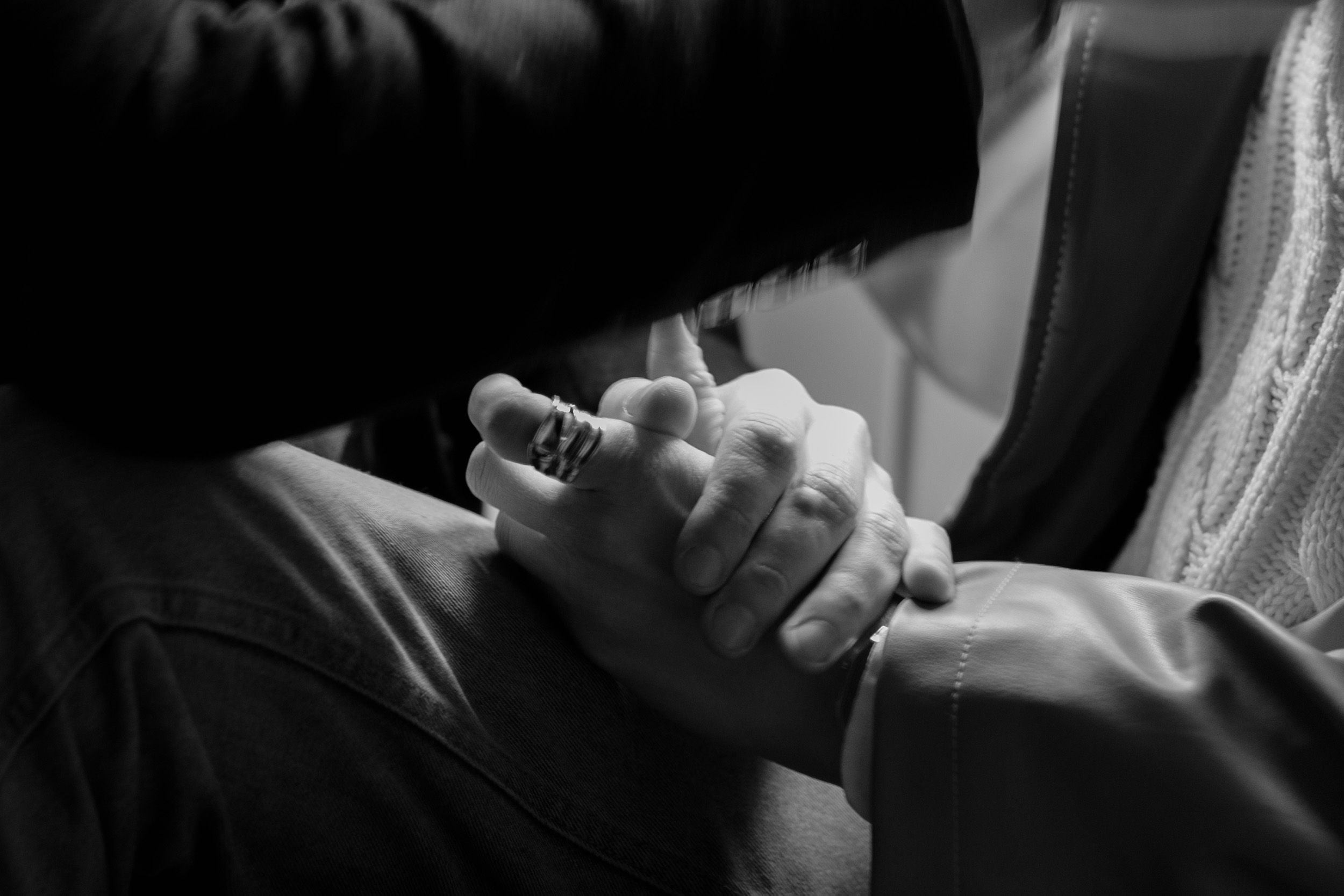 A black and white photo shows two hands clasped together in an intimate moment of prayer or connection.
