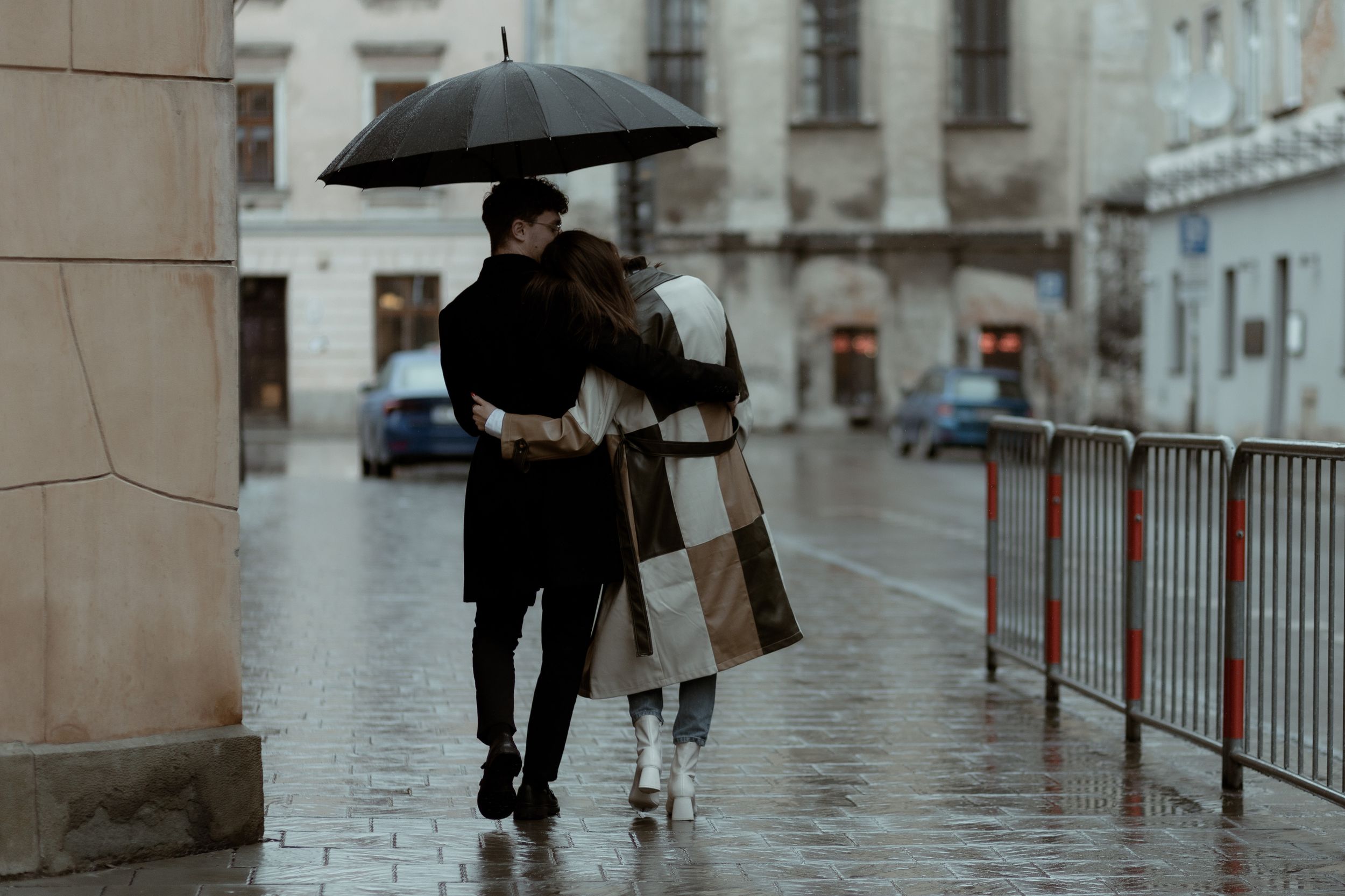 A couple shares an umbrella while walking together in the rain on a cobblestone street during a moody winter day.