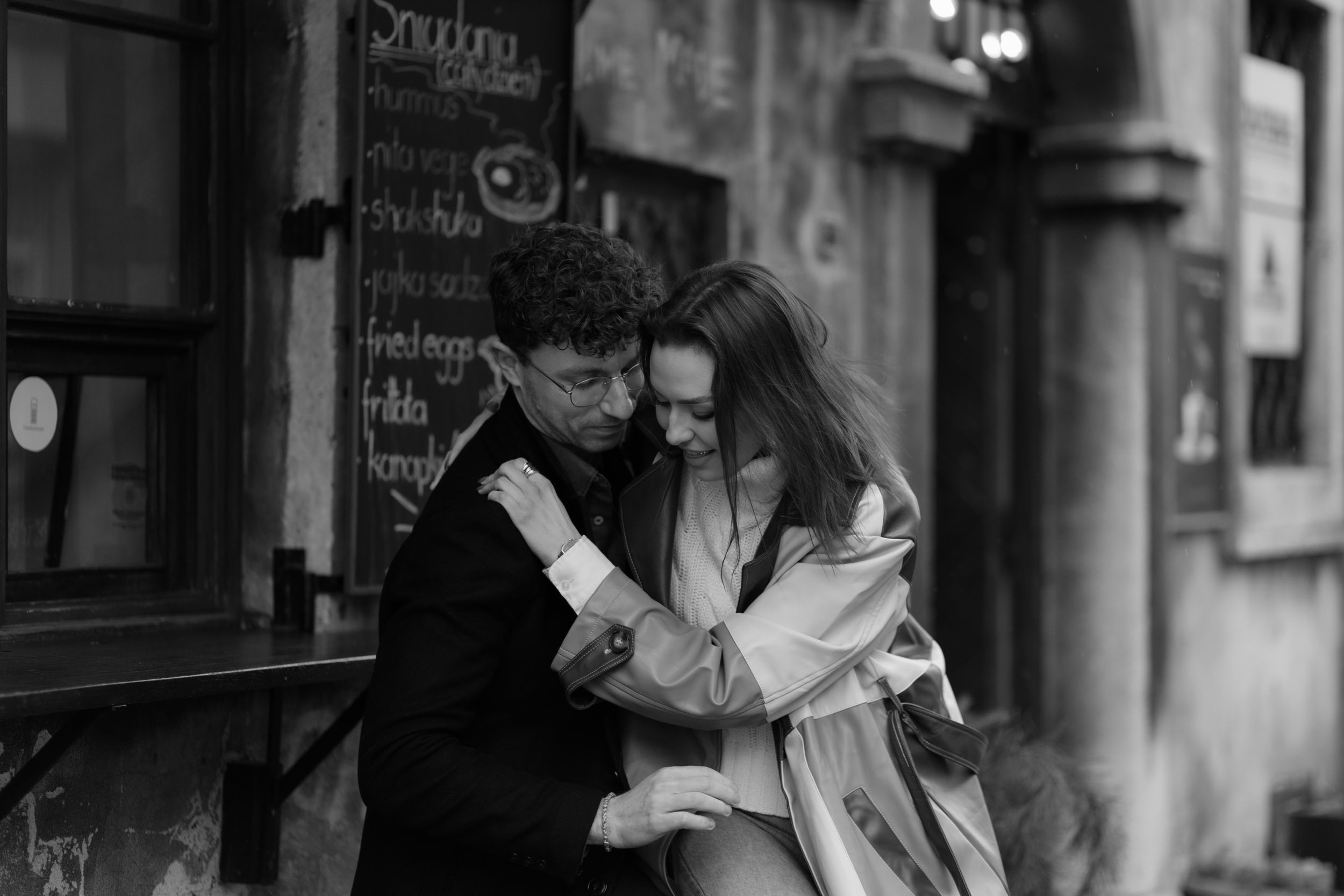A romantic black and white moment captured between a couple embracing outside a cafe in the city.