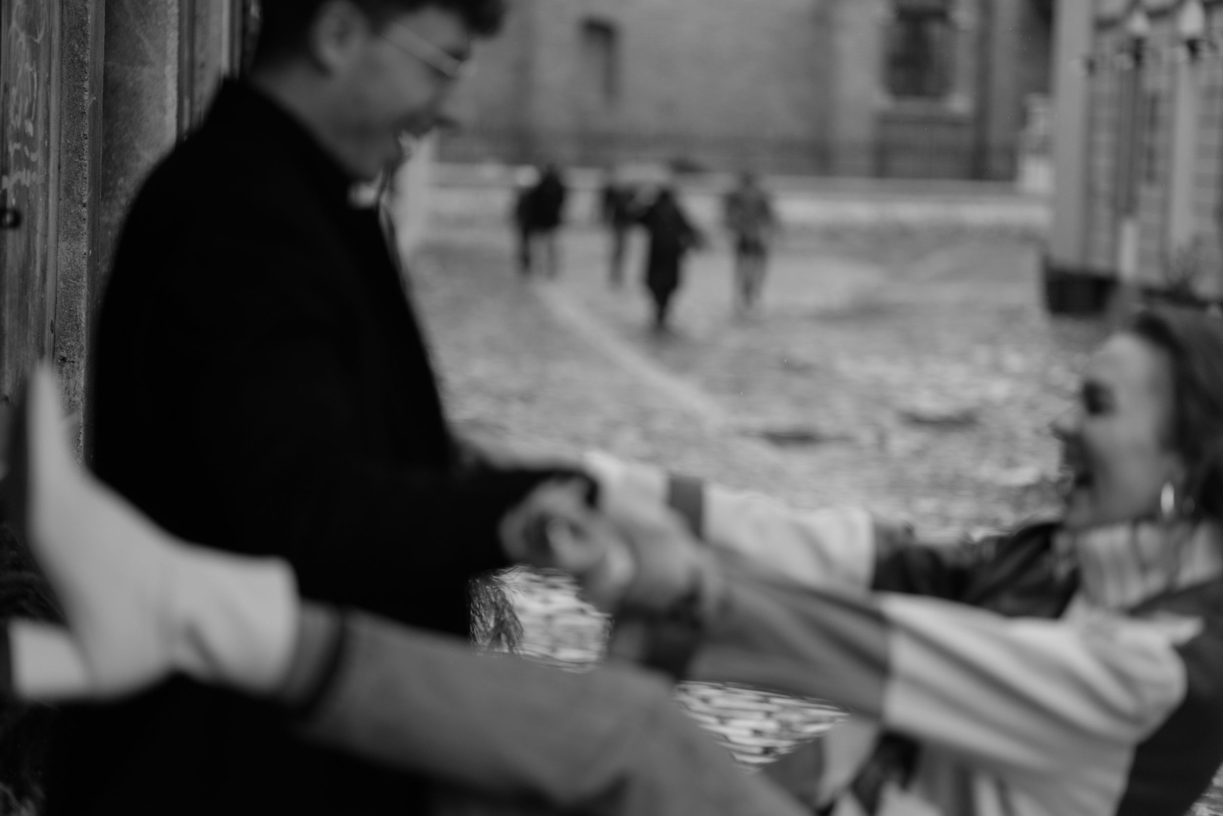 Blurred black and white image shows hands arranging items at an outdoor market or street vendor stall.