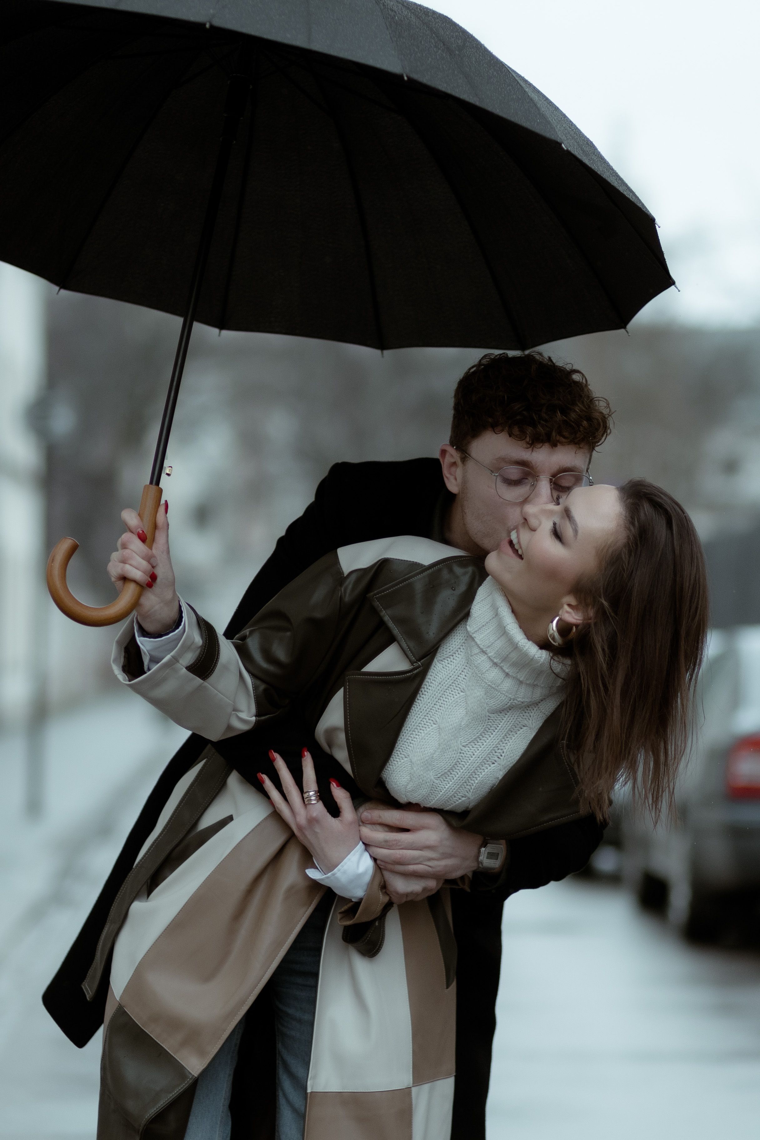 Romantic couple sharing an intimate moment under a black umbrella on a moody rainy day.