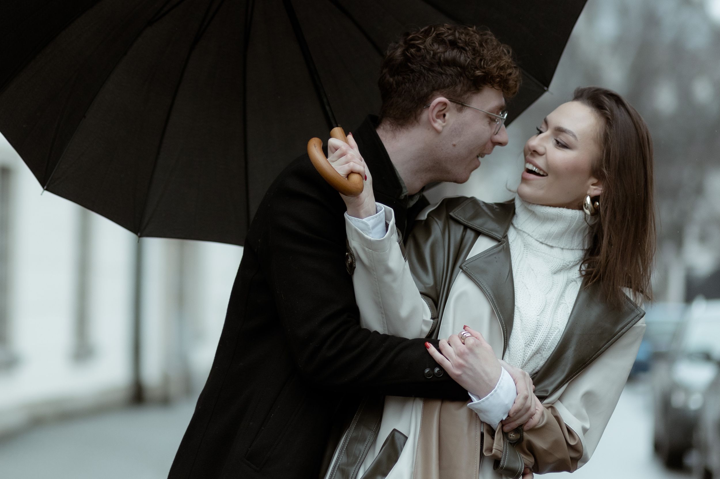 A romantic couple sharing a tender moment under a black umbrella on a gloomy day.