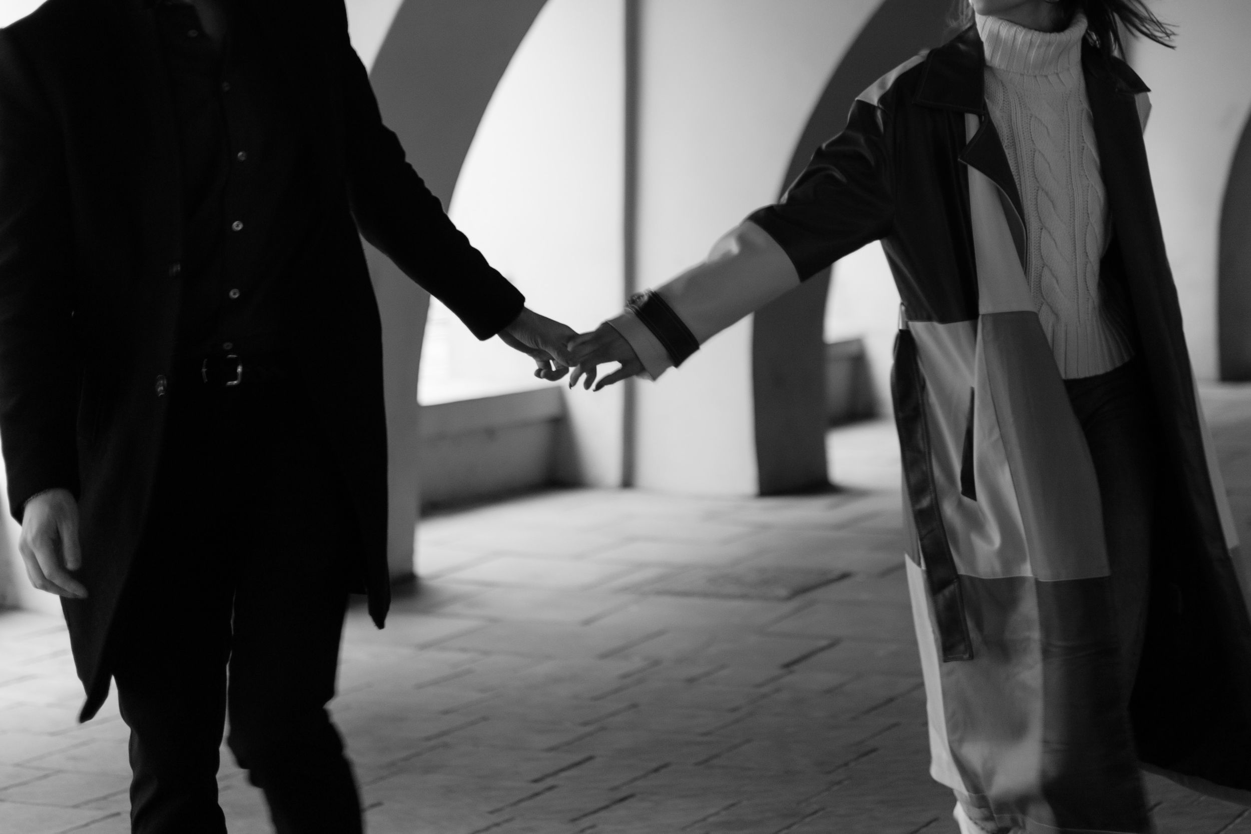 Black and white photo showing two people holding hands in a corridor with dramatic shadows.