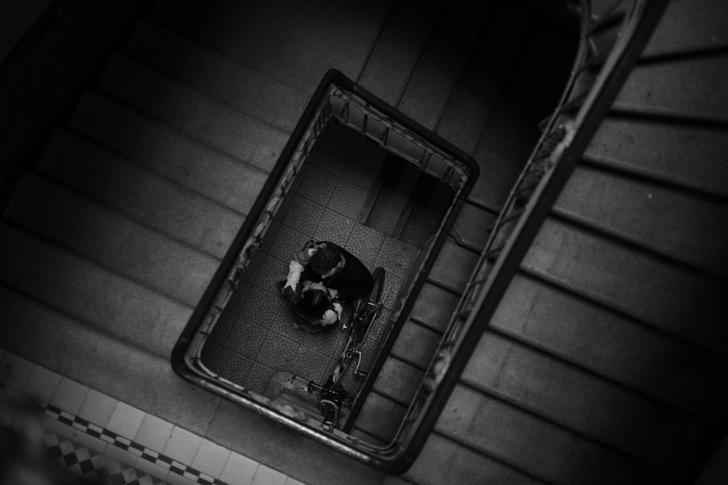 A black and white aerial view looking down a spiral staircase with a figure standing at the bottom.