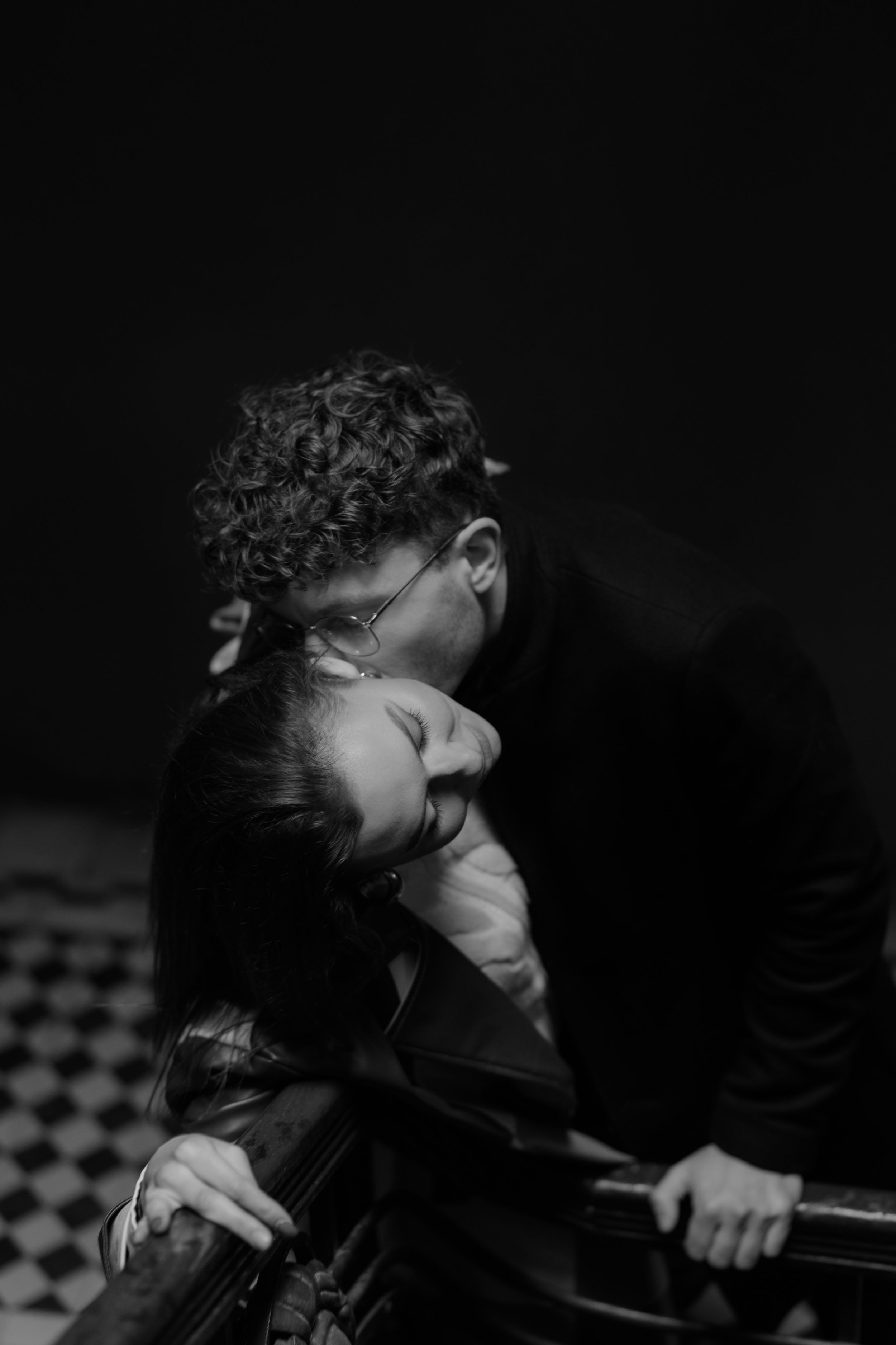 An artistic black and white photo capturing an intimate moment on a dark checkered tile floor.