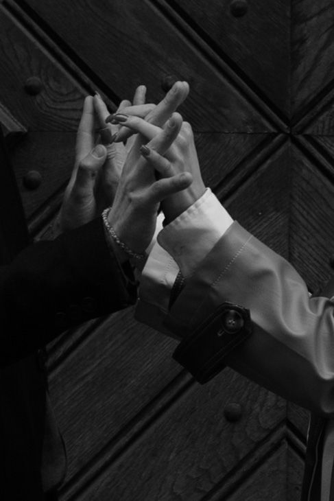 Black and white photo of hands intertwined in an artistic pose against a textured wooden door background.
