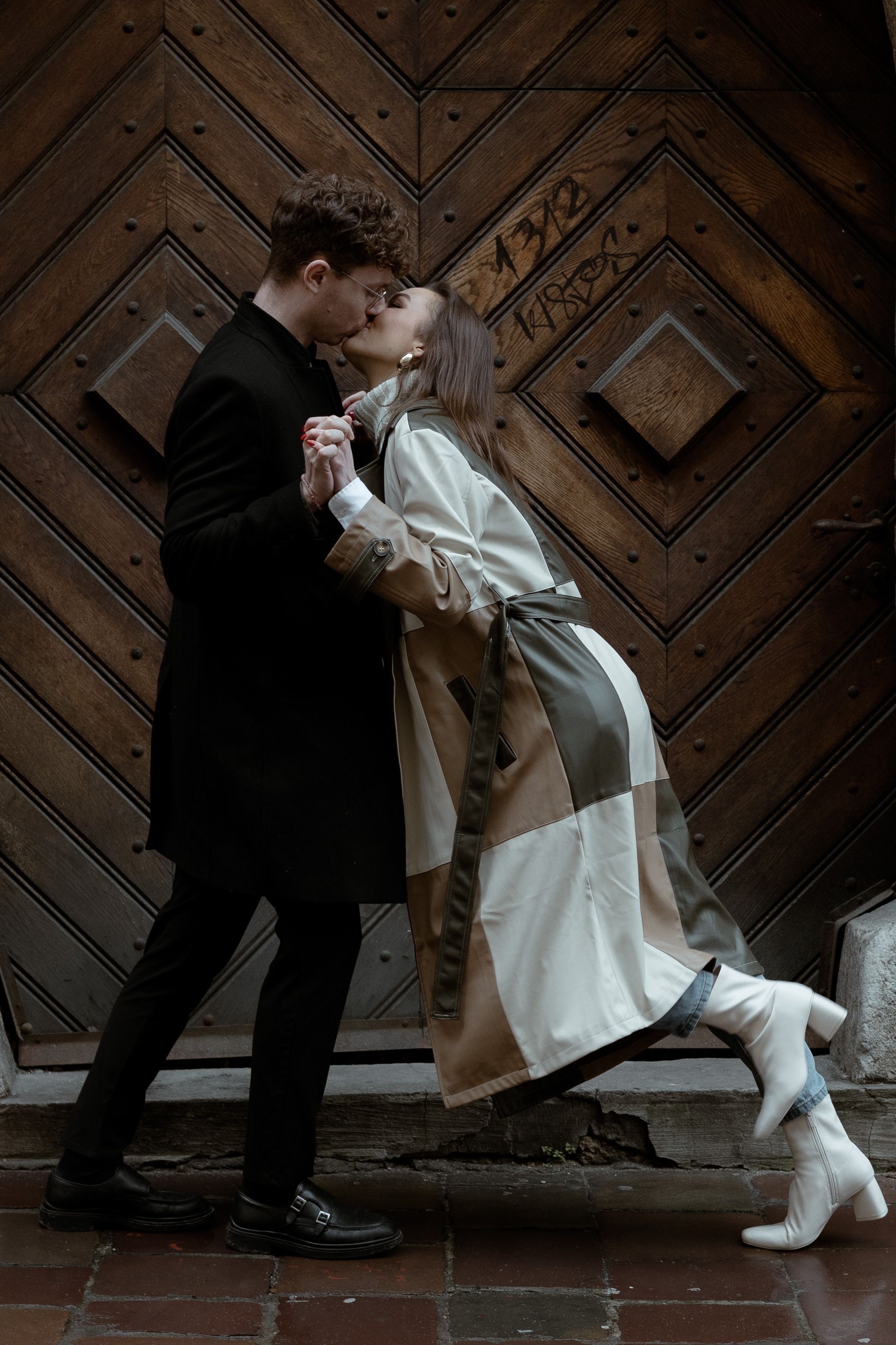 A romantic couple in vintage attire shares an intimate moment against an ornate wooden door.