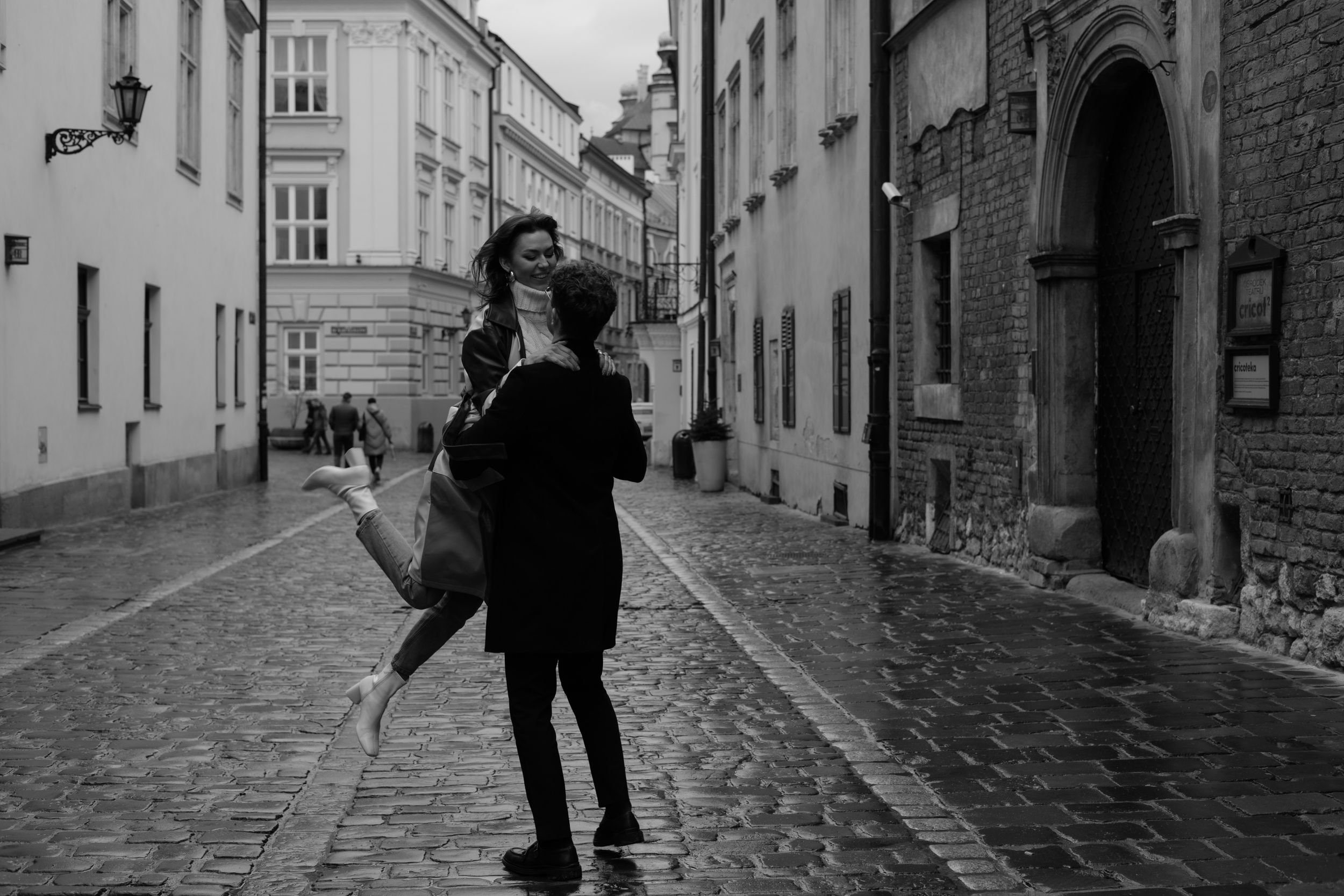 A silhouette stands on a cobblestone street between historic buildings in an old European city quarter.