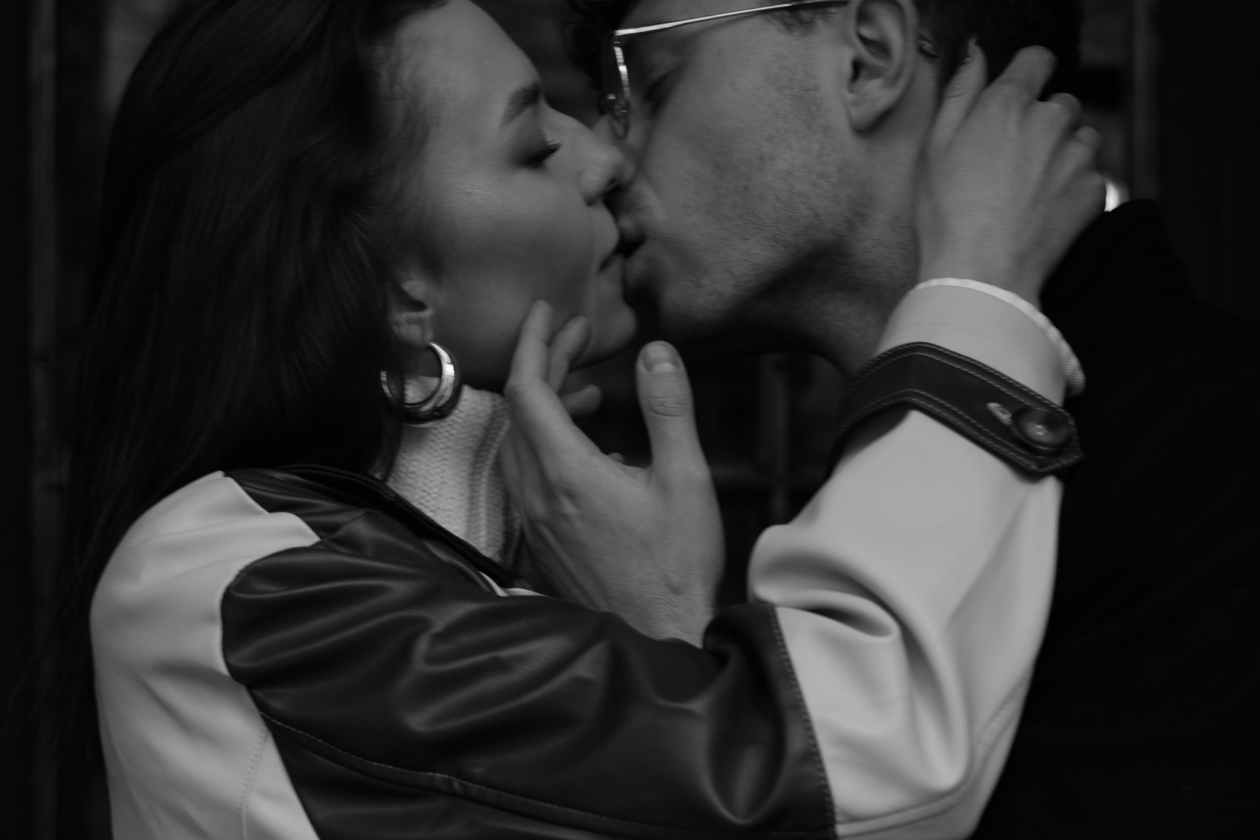 A romantic black and white photograph captures an intimate kiss between two people wearing formal attire.