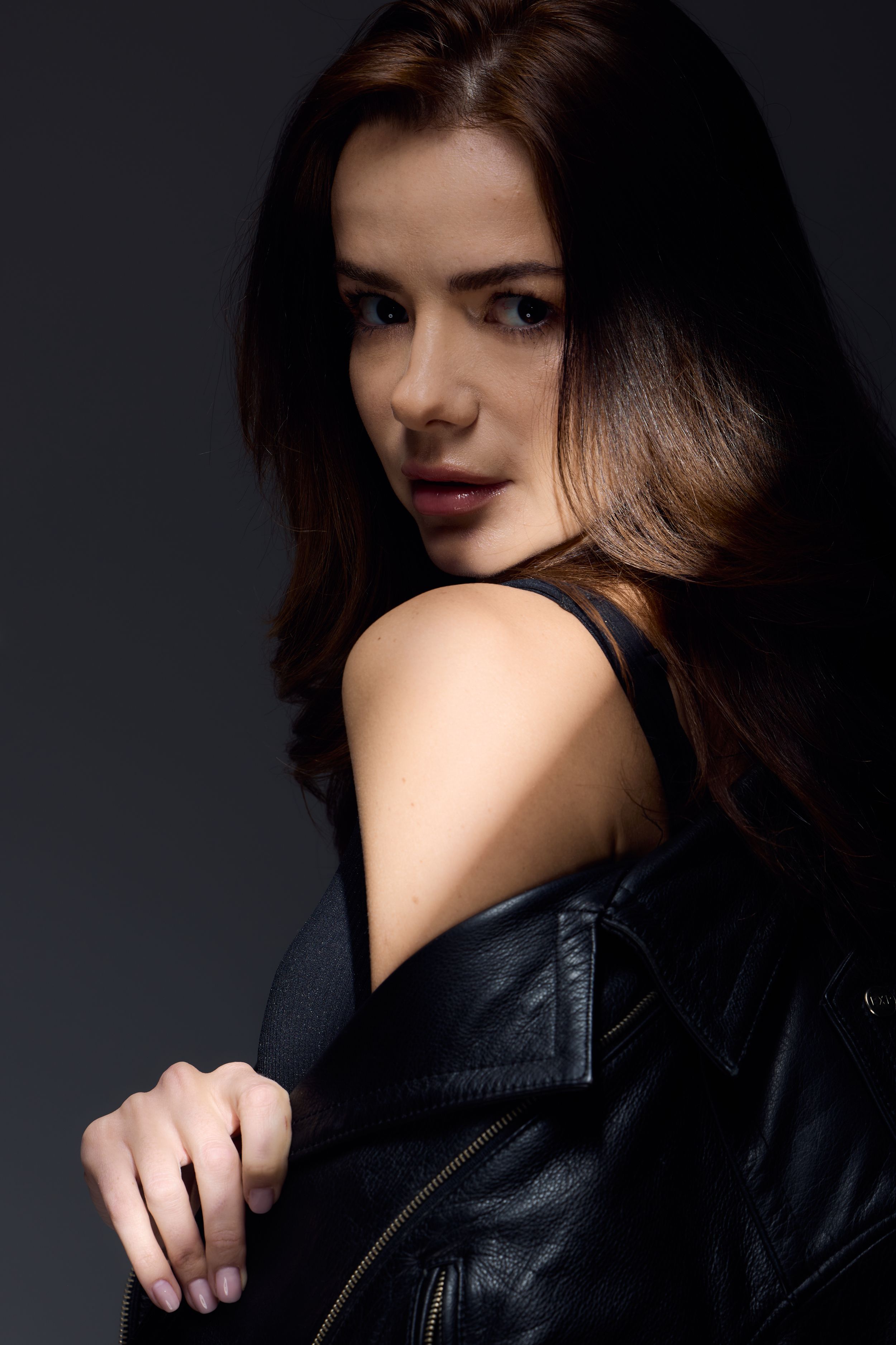 Dramatic studio portrait of someone in a black leather jacket looking over shoulder against dark background.