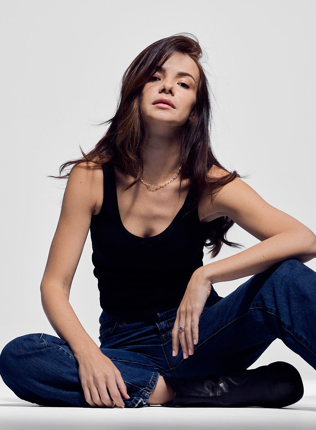 Fashion portrait of model in black tank top and jeans posing against white backdrop.