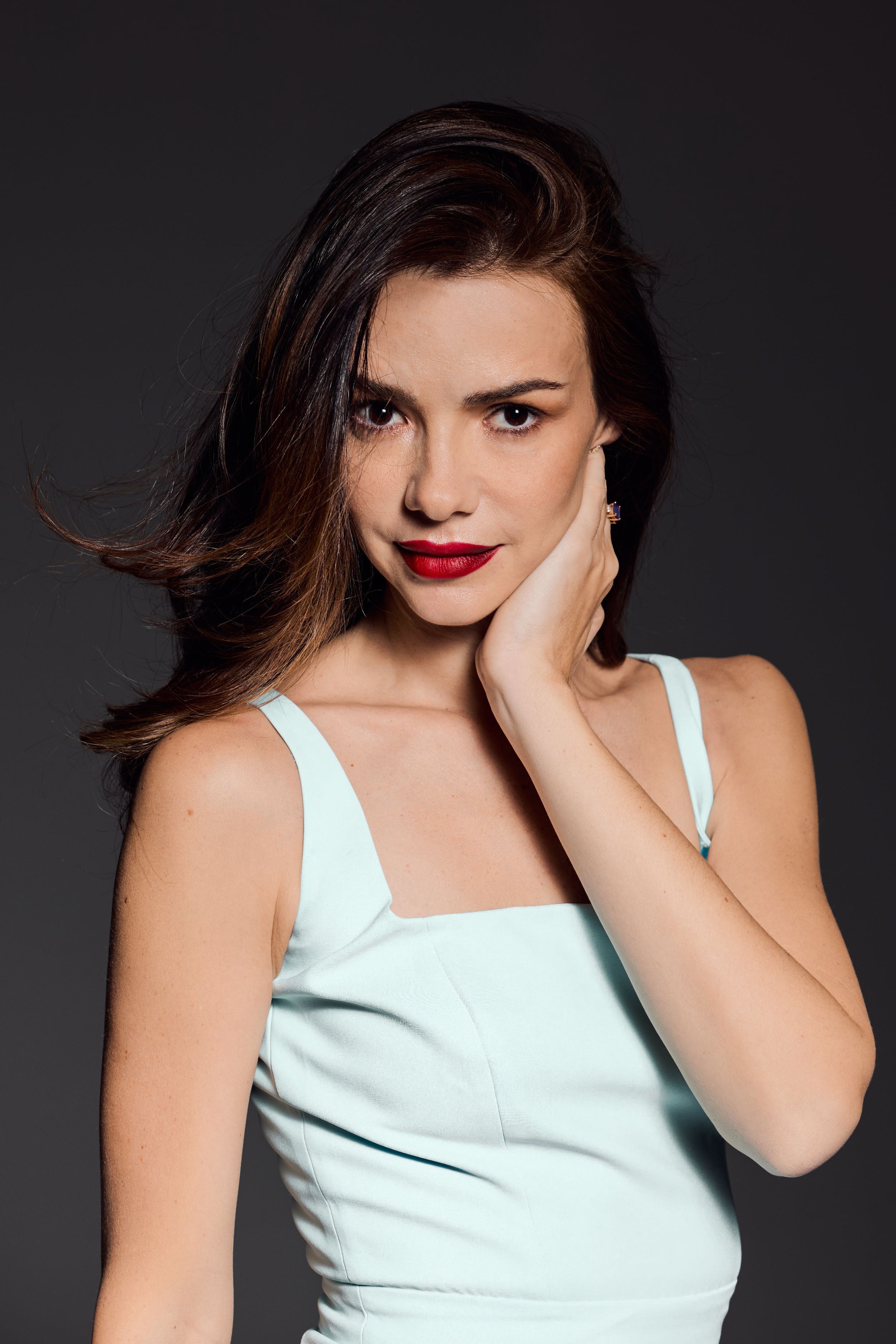 Portrait against dark background of a model in a mint green tank top with flowing dark hair and red lipstick.