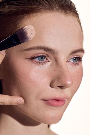 Applying makeup with a large brush while showcasing natural-looking foundation and subtle eye makeup.