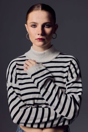 Portrait of someone wearing a striped black and white turtleneck sweater with hoop earrings against a dark background.