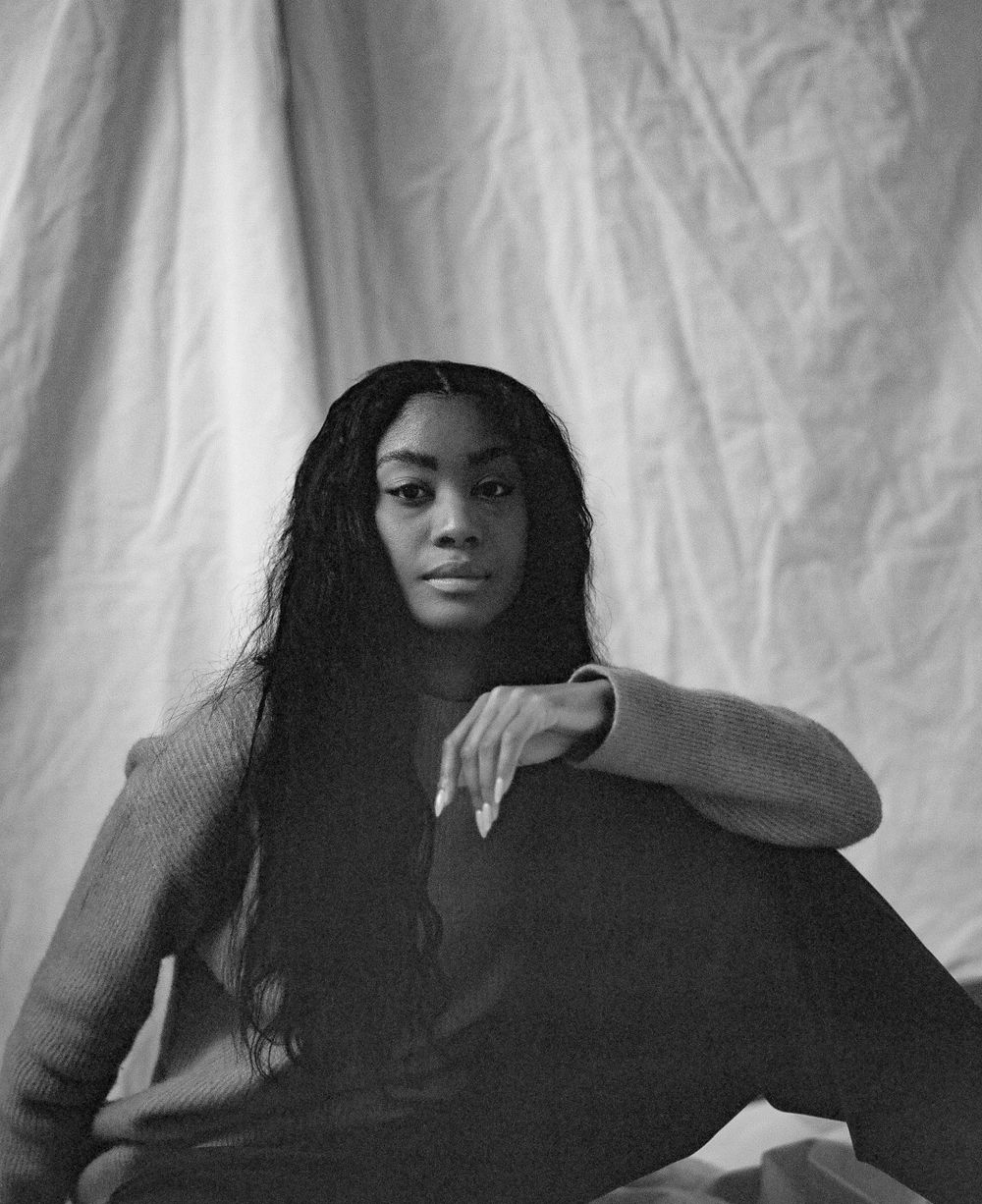 Black and white portrait of a person wearing dark clothing against a white fabric backdrop.