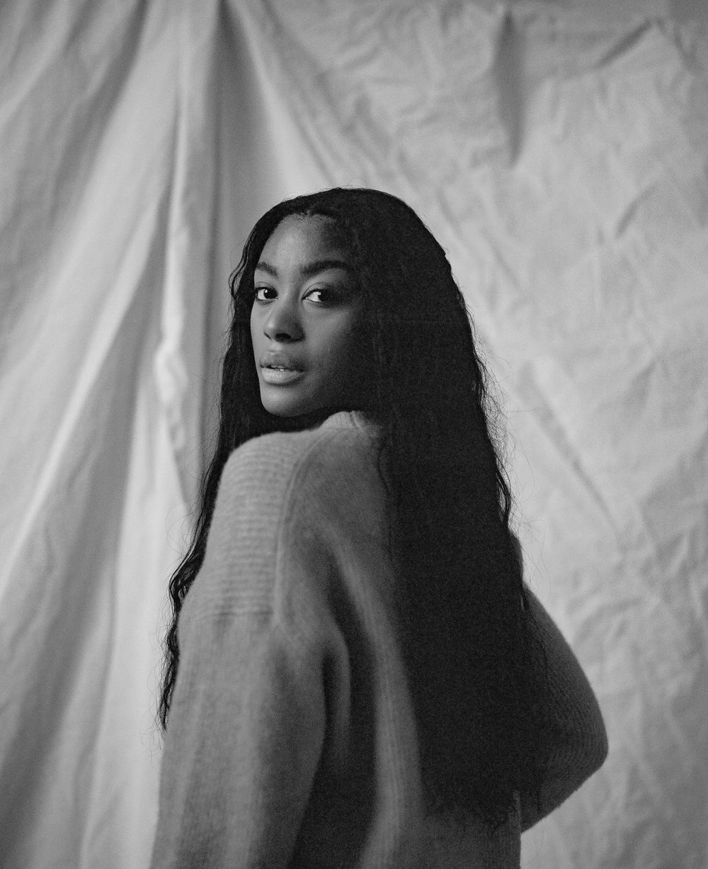 Black and white fashion portrait with long hair against white fabric backdrop.
