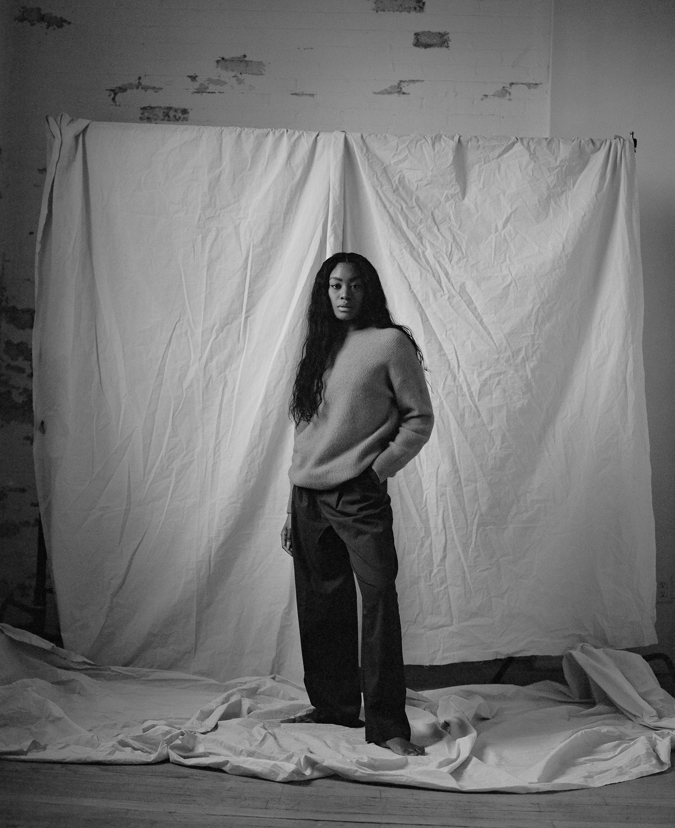 Portrait shot against white backdrop showing a casual pose in monochromatic tones.