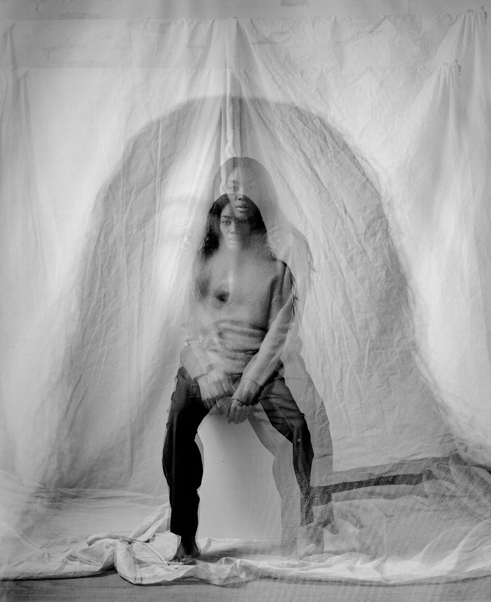 Artistic black and white portrait against white backdrop with ethereal double exposure effect.