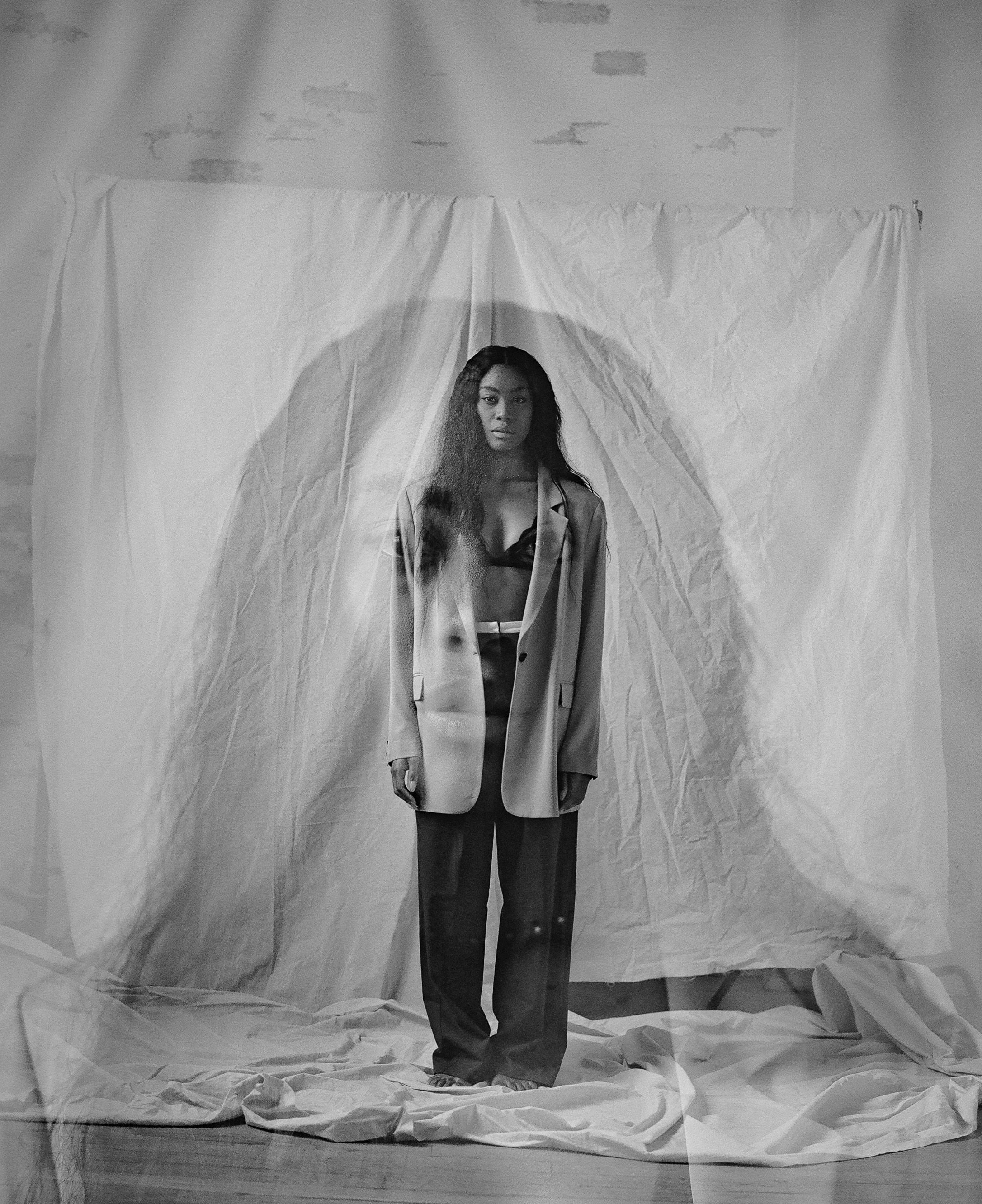 Minimalist fashion portrait with oversized blazer against draped white backdrop.