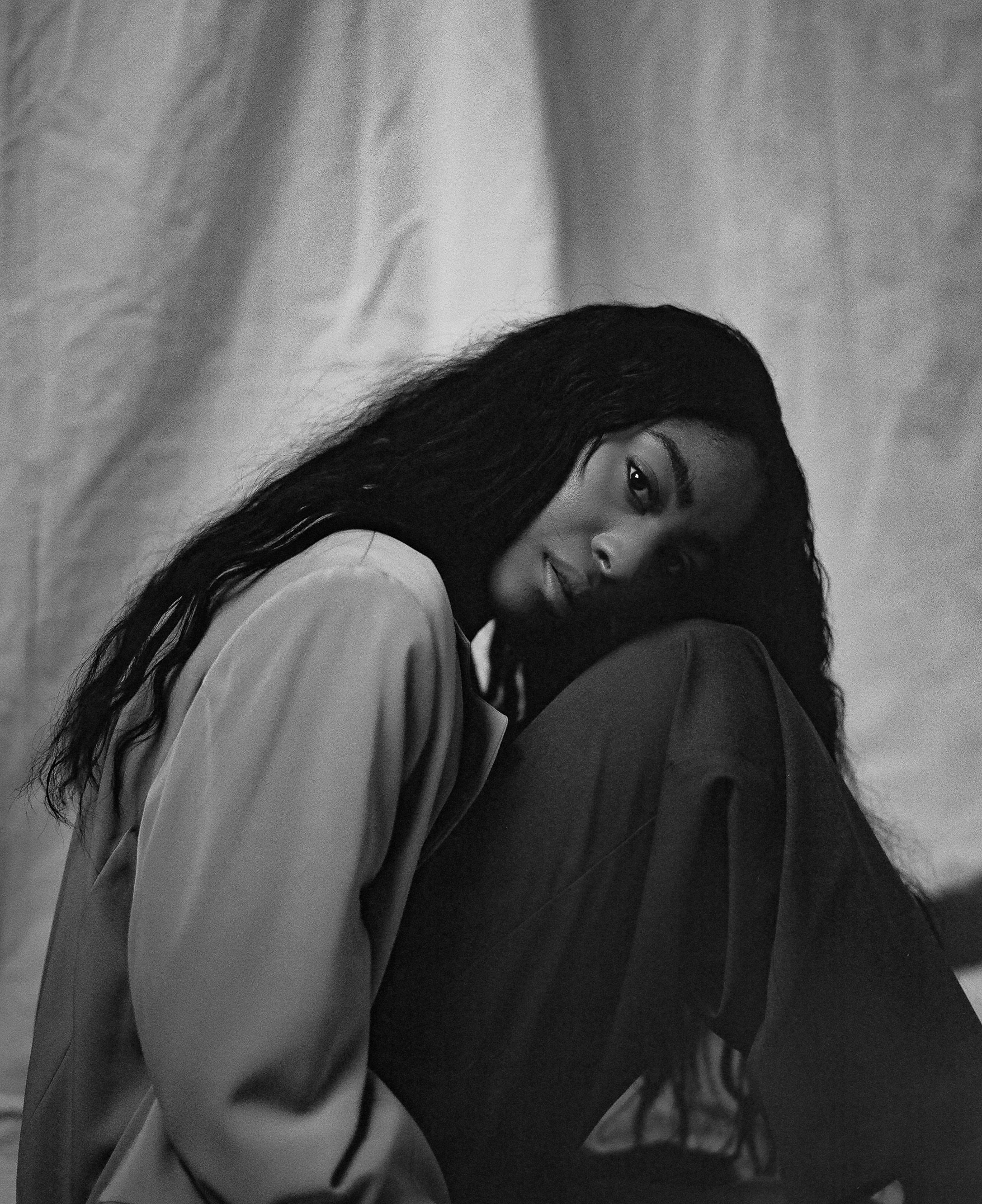 Moody black and white portrait in relaxed pose wearing loose clothing.