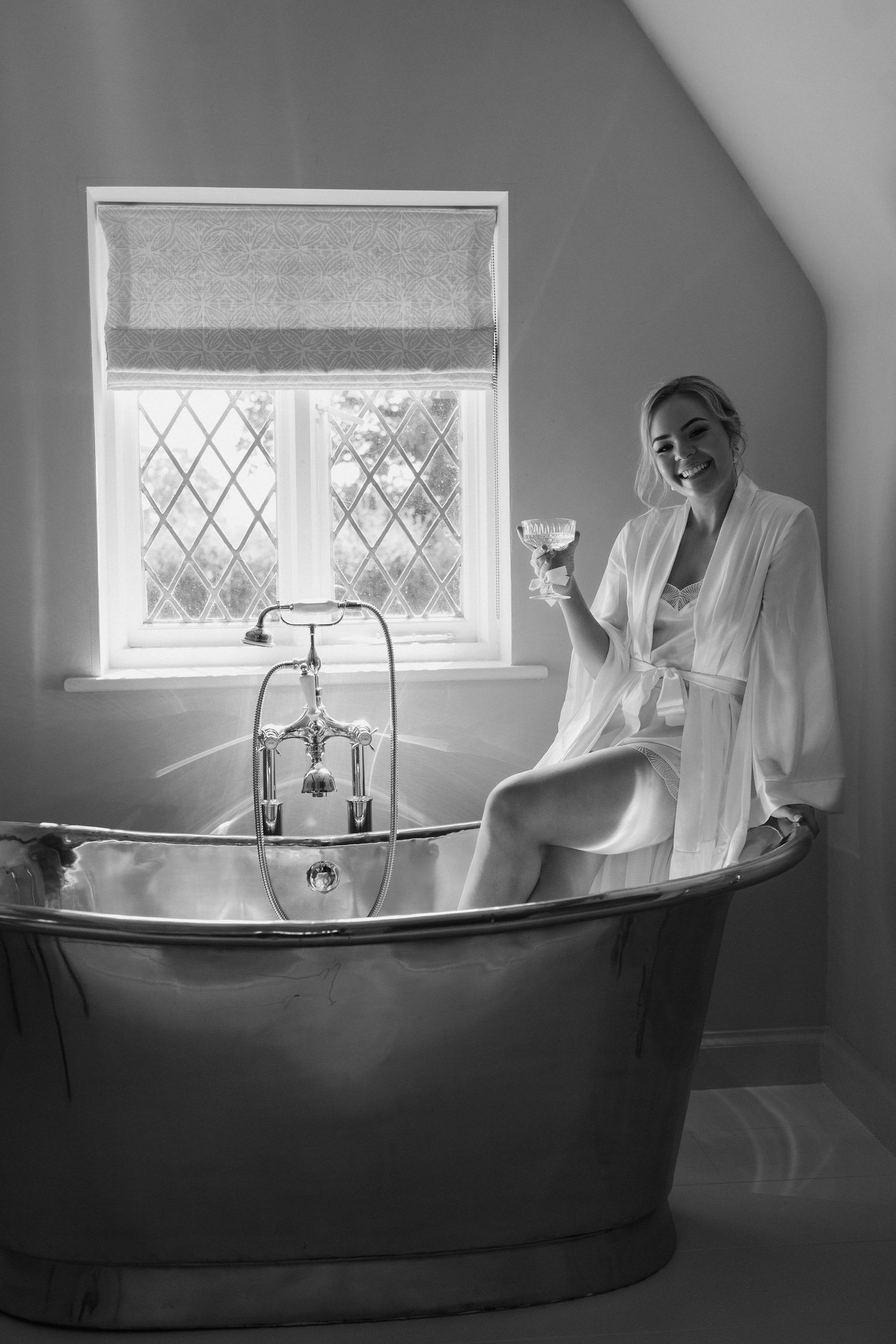 bride sitting on edge of bath tub with champagne in hand in the cottage at Iscoyd park