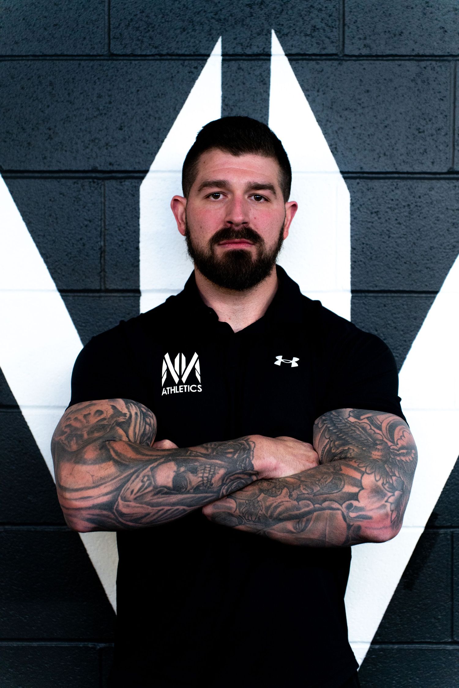 Athletic trainers in black hoodies display tattooed arms against geometric backdrop.