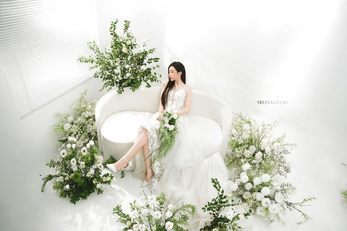 Ethereal white studio setting with curved chairs and delicate floral arrangements creating a dreamy bridal atmosphere.