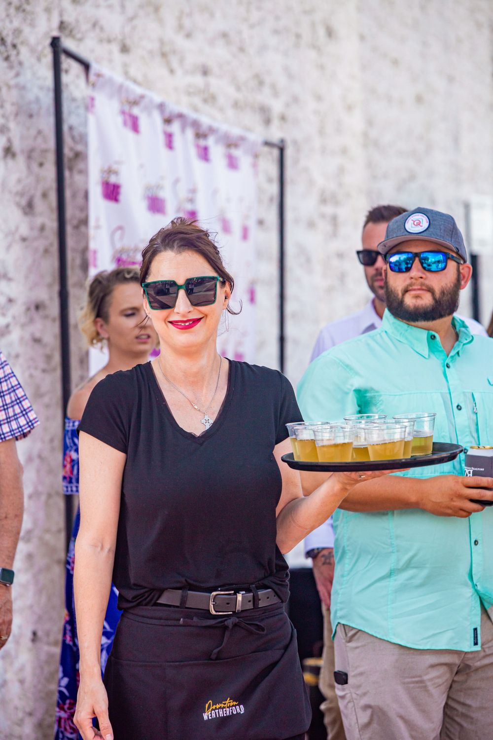 Service staff carrying trays of drinks at an outdoor event.