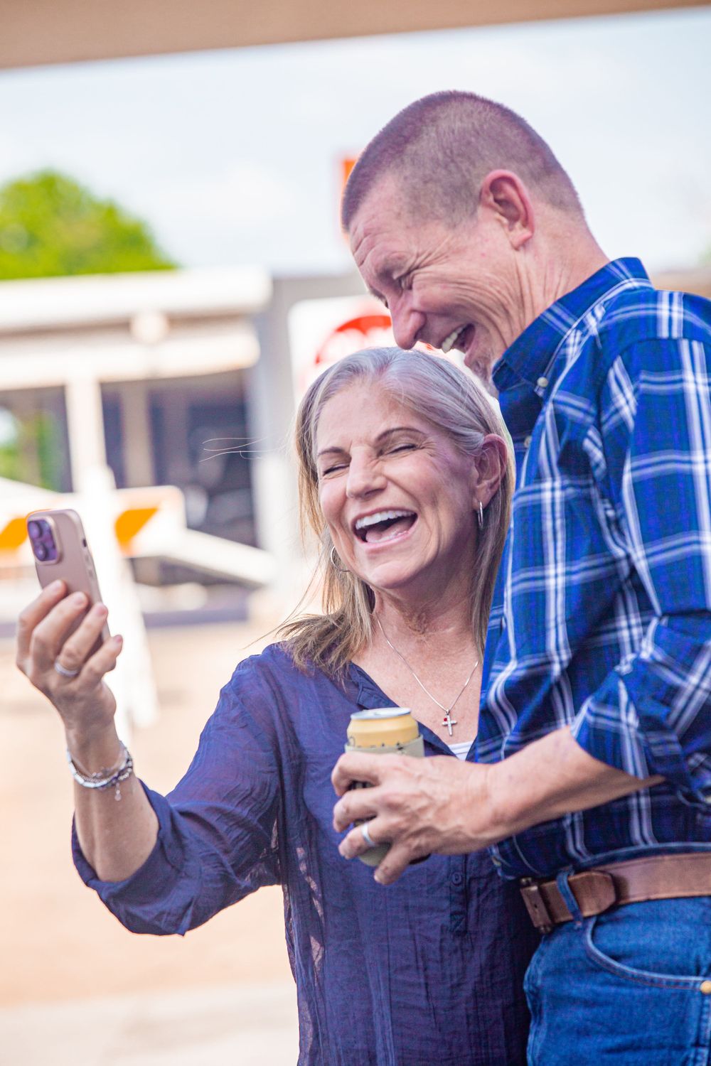 Friends sharing laughs while holding beverages at an outdoor event.