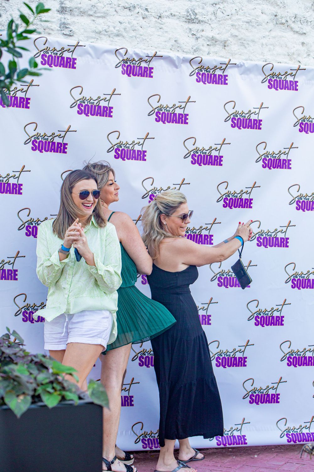 Group of friends posing playfully in front of a branded photo backdrop.