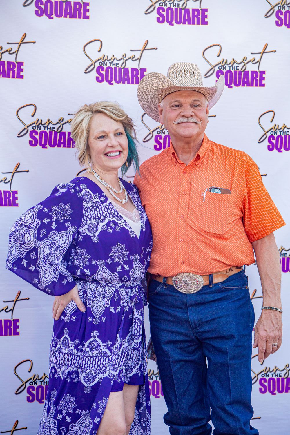 Couple posing in front of a purple and white branded backdrop at an event.